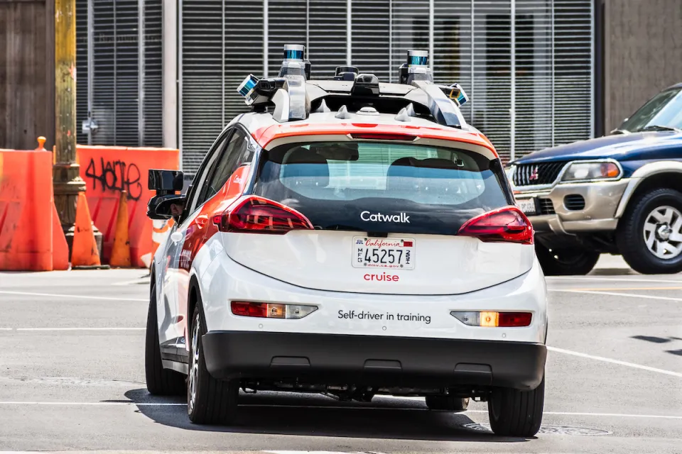 White and red Cruise self-driving car with "Self-driver in training" sign on back